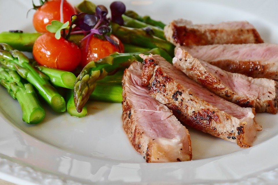 on a white plate, cherry tomatoes and asparagus are delicately placed next to a medium-rare veal chop, sliced thin and fanned 
